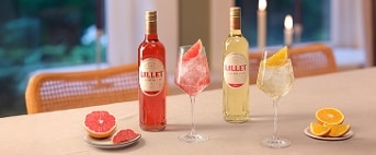 Flessen Lillet rosé en blanc met bijpassende cocktails in glazen, geserveerd met schijfjes grapefruit en sinaasappel op een eettafel, met Royal van Kempen & Begeer servies.