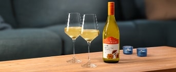 Fles Lindeman's Chardonnay witte wijn met twee glazen op een houten salontafel, voor een blauwe bank