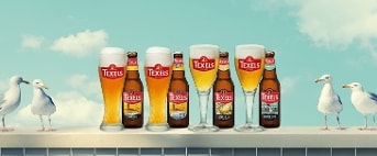 Texels speciaalbier flessen en glazen op een muurtje met meeuwen en een vuurtoren op de achtergrond.