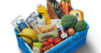 Blauwe Albert Heijn krat gevuld met boodschappen zoals brood, melk, croissants, bananen, sinaasappelsap, broccoli, tomaten, kaas, eieren en wortels
