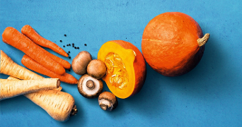 Pompoen, wortels, paddenstoelen en pastinaken op een blauwe achtergrond.