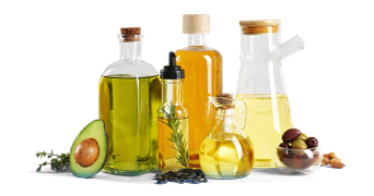 Verschillende soorten olie in glazen flessen, samen met een halve avocado, kruiden, olijven en noten.