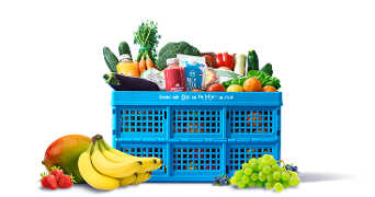 Blauwe Albert Heijn krat vol verse groenten, fruit en zuivelproducten, met op de voorgrond bananen, mango, aardbeien, en groene druiven.