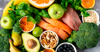 Verscheidenheid aan verse en gezonde voedingsmiddelen waaronder appel, avocado, peer, banaan, sinaasappel, grapefruit, broccoli, blauwe bessen, zalmfilet, kipfilet, notenmix, linzen, havermout en groene bladgroenten.