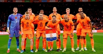 Voetbalelftal van Nederland poseert in oranje tenue op het veld voor een groepsfoto tijdens een interlandwedstrijd.