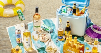 Picknick op het strand met verschillende frisdrank- en alcoholische dranken van A-merken zoals Sprite, Birra Moretti, Crodino en Saint Roche, geserveerd op een kleed met snacks en koelbox.