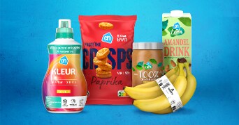 Albert Heijn producten op een blauwe achtergrond, waaronder AH kleur wasmiddel, AH paprika crisps, AH Terra 100% pindakaas, AH Terra amandeldrink en een tros bananen.