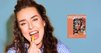 Portret van Veggilaine die lacht en haar kookboek op een blauwe achtergrond