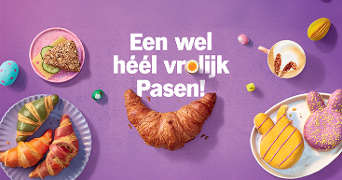Paasontbijt met gevulde en gekleurde croissants, paasbroodjes in vorm van haas, een volkoren boterham met komkommer, gekleurde paaseieren, een kop koffie en een glas sinaasappelsap op een paarse ondergrond met de tekst "Een wel héél vrolijk Pasen!"