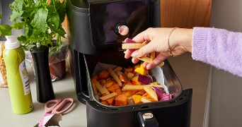 Vrouw die groentefrietjes in een airfryer legt in een keuken.