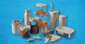 Verschillende beige voorraadbussen, containers en drinkbekers van kunststof en glas, gevuld met etenswaren zoals koekjes, ontbijtgranen, koffiebonen en zaden, samen met afsluitclips en een doseerlepel, uitgestald op een blauwe achtergrond.