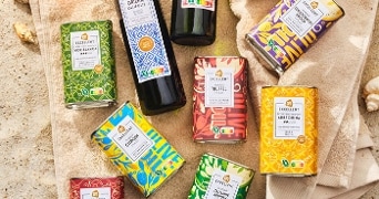 Albert Heijn Excellent olijfolie en kleurrijke conserverblikken op een zandstrand met schelpen op de achtergrond.