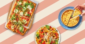 Rechthoekige pizza met groenten, kleurrijke pastasalade en een hand die een stukje quiche pakt.