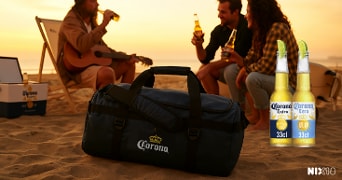 Groep mensen zit op het strand met flesjes Corona bier in de hand, een Corona sporttas en koelbox op de voorgrond, twee flesjes Corona (Extra en Cero) prominent rechts in beeld, bij zonsondergang
