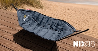 Zwarte Fatboy hangmat met Corona-logo op een houten terras bij het strand, met NIX18-logo rechtsonder in beeld.