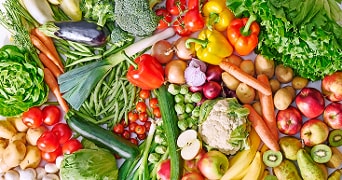 Assortiment van verse groenten en fruit zoals paprika, broccoli, wortels, appels, tomaten, sla, bananen, kiwi en courgette.