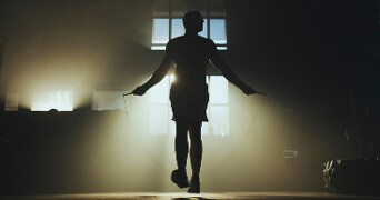 Silhouet van een sporter die touwtje springt in een fitnessruimte met achterlicht