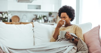 Persoon drinkt koffie op de bank onder een deken in een gezellige woonkamer.