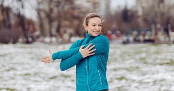 Persoon in sportkleding die buiten een warming-up stretch oefening doet in een park met lichte sneeuw op de grond