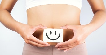 Vrouw met een lachend gezichtje op haar buik, symbool voor welzijn of gezondheid.
