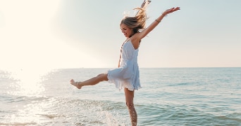 Vrouw in witte jurk geniet van de zonsondergang aan zee.