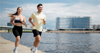 Twee mensen die hardlopen langs het water met een modern gebouw op de achtergrond