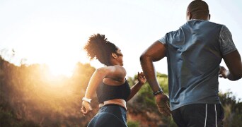 Twee mensen aan het hardlopen buiten met de zon op de achtergrond.