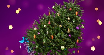 Kerstboom versierd met kleurrijke ornamenten in een winkelwagentje op een paarse achtergrond, beschikbare kerstbomen bij Albert Heijn.