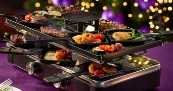 Gourmetstel gevuld met verschillende soorten vlees, vis en groenten, feestelijk gepresenteerd op een gedekte tafel met kerstverlichting op de achtergrond