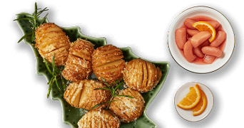 Geroosterde hasselback aardappelen met rozemarijn op een groene serveerschaal in de vorm van een kerstboom, geserveerd met een schaaltje gepocheerde peren en een schoteltje sinaasappelpartjes