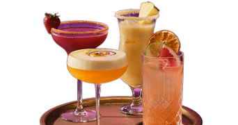 Vier kleurrijke cocktails in verschillende glazen op een dienblad, elk versierd met fruit zoals aardbei, ananas, passievrucht en sinaasappel