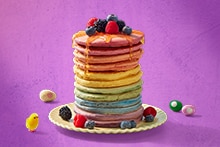 Stapel kleurrijke pannenkoeken op een bord, gegarneerd met honing en verse bessen zoals frambozen, bramen en blauwe bessen.