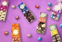 Verschillende verpakkingen Delicata paaseitjes en chocolade, verspreid met losse paaseitjes in diverse kleuren op een zwarte achtergrond