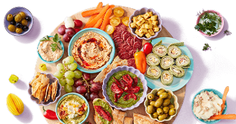 Borrelplank met diverse hapjes waaronder hummus, tapenade, druiven, olijven, groente, kaasblokjes, crackers, wraps en vleeswaren.
