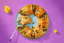 Diverse paasgerechten op tafel, waaronder gevulde eieren, een schaal met sesamtonijn op groenten, krokant brood en een hartige taartkrans.