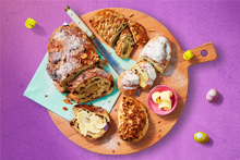 Ontbijttafel met verschillende soorten broodjes, croissants, gesneden brood met rozijnen, een gekookt ei, sinaasappelsap, cappuccino en boter.