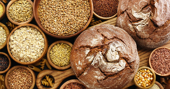 Twee ronde broden met een krokante korst, omringd door verschillende kommen gevuld met diverse soorten granen en zaden.