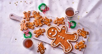 Gemberkoekjes en mokken thee op een houten serveerplank met kerstdecoraties.
