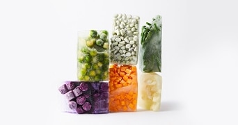 Blokken van diverse soorten bevroren groenten en fruit, waaronder spruitjes, doperwten, sperziebonen, rode bessen, wortels en bloemkool.