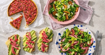 Tartaart met rode groenten, salade met groene groenten, en sneetjes brood belegd met kaas, komkommer en ingemaakte rode groenten, gepresenteerd op een tafel.