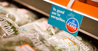 Voorverpakte zakken gesneden boerenkool in het koelschap bij Albert Heijn, met een bordje “Te goed om te verspillen” en “Laatste kans koopjes”.
