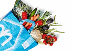 Gekleurde tas van Albert Heijn gevuld met verse groenten, zoals spinazie, paprika's, wortels, avocado's, bloemkool, en tomaten.