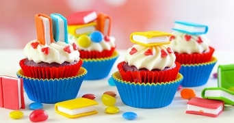 Cupcakes versierd met gekleurde marsepeinen boeken, hartjes en snoepjes, op een feestelijke achtergrond