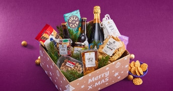 Feestelijk kerstpakket van Albert Heijn gevuld met diverse lekkernijen zoals bier, wijn, kaas, crackers, chocolade, nootjes en andere feestelijke snacks, gepresenteerd in een doos met de tekst 'Merry X-Mas'.