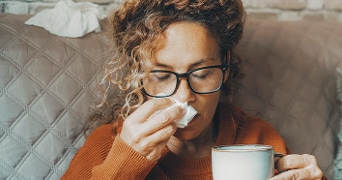 Persoon in een gezellige setting met een kop warme drank op een bank.