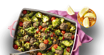 Ovenschotel met gehaktballen, broccoli, kikkererwten en cherrytomaatjes, geserveerd met partjes citroen.