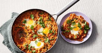 Shakshuka met eieren en verse kruiden in een koekenpan en op een bord.