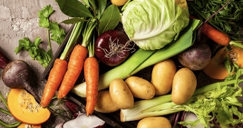 Verse groenten, waaronder wortels, aardappelen, prei, pompoen, rode ui, witte kool en selderij op een rustieke ondergrond