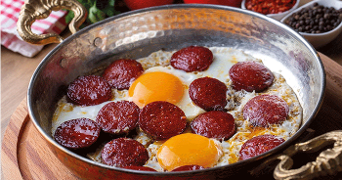 Gebakken eieren met plakjes sucuk in een koperen pan.
