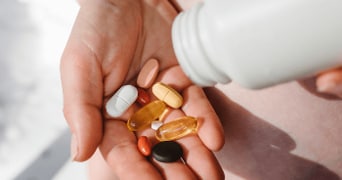 Hand met verschillende soorten pillen en vitamines uit een flesje.